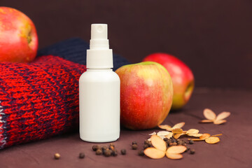 cosmetic spray bottle, autumn apples, sweater and dry hydrangea flowers on dark brown background....