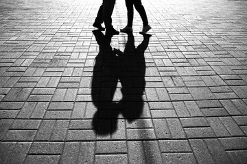 A black and white shadow on the pavement of a man and woman kissing