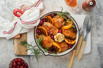 Fototapeta na wymiar Baked chicken thighs with orange, cranberry and spicy herbs rosemary servered in frying pan on light background. Festive Christmas Dinner Concept menu. Top view. copy space