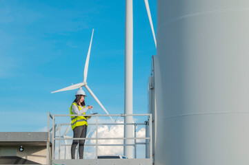 women engineer working and holding the report at wind turbine farm Power Generator Station on mountain,Thailand people