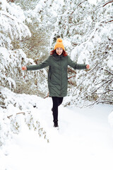 Cheerful girl in warm clothes playing with snow outdoors near the beautiful forest