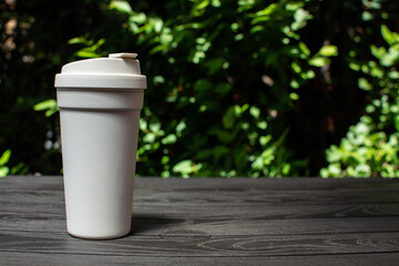white coffee cup on black wooden table with green leaves background