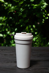 Obraz premium white coffee cup on black wooden table with green leaves background