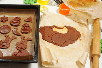 Gingerbread cookies squeezed out of rolled dough using stencils lie in a tray ready to bake.
