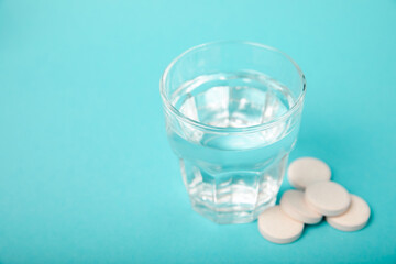 An effervescent vitamin tablet drops and dissolves in a glass of water on a blue background. The concept of health. Medicine concept. Place for text.