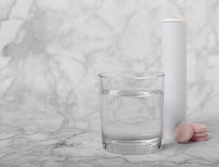Vitamin C effervescent tablets with orange flavor drops and dissolves in a glass of water on a white marble background. The concept of health. Medicine concept. Place for text.