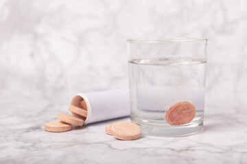 Vitamin C effervescent tablets with orange flavor drops and dissolves in a glass of water on a white marble background. The concept of health. Medicine concept. Place for text.