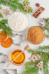 Obraz na płótnie Canvas Top view of ingredients for baking of gingerbread biscuit dessert such as honey, flour, sugar and cinnamon arranged on white wooden table with cookie cutters, fir tree branches and christmas decor