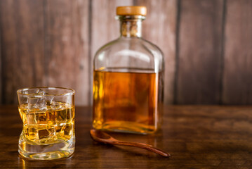 A glass of whiskey with ice cubes,with a bottle with whiskey in the background out of focus,on wooden background.
