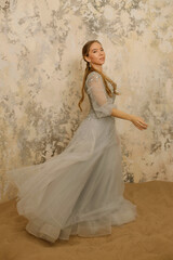 a girl in a dress on the sand against a shabby wall