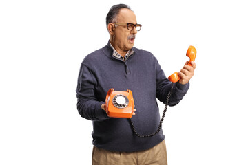 Confused mature man holding a vintage rotary phone and looking at the handset