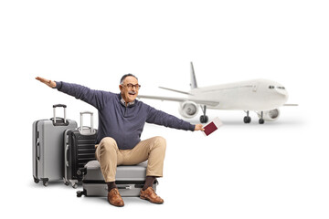 Mature man sitting on a suitcase with a passport and a ticket and spreading arms to fly