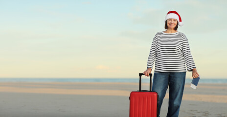 Banner of happy adult woman in Christmas Santa hat with red suitcase, passport boarding pass ticket...