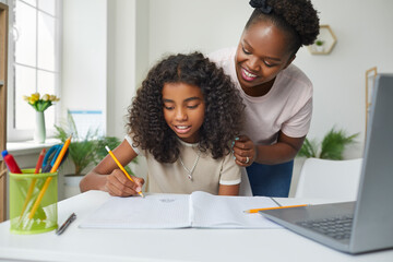 Happy family doing homework. Supportive African American mother helping her creative daughter while...