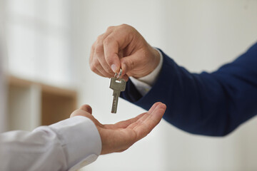 Key exchange. Close up unrecognizable male real estate agent handing key to new owner of apartment....