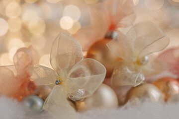 Christmas or New Year festive blurred background with beige bows and balls on white snow. Shallow depth of field. Beautiful bokeh. Airy atmosphere. 