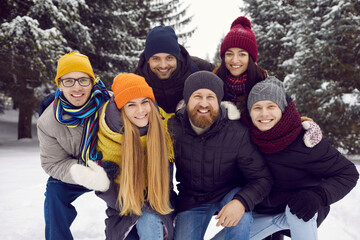 Bunch of cheerful millennial friends having fun outside in the winter time. Happy young people in warm winter clothes posing for a group photo in a beautiful snowy park or forest