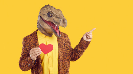 Portrait funny man in crazy T Rex dinosaur face mask and funky leopard jacket standing on yellow...