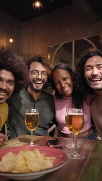 Vertical video of a Portrait of A group of friends looking at camera in the restaurant bar after work at the pub happy hour. Happy friends having fun together drinking alcohol indoors.