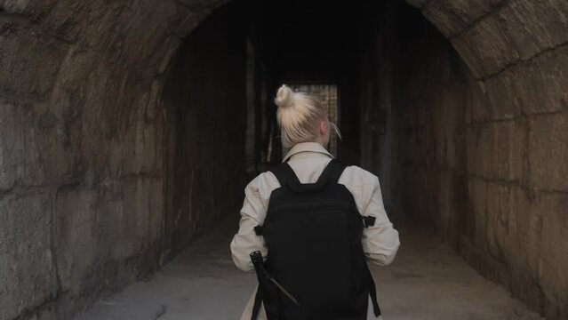 A young female archaeologist or student enters an ancient corridor inside the amphitheater and studies the ancient ruins looking at the walls and at the ceiling. A female explorer 4k footage