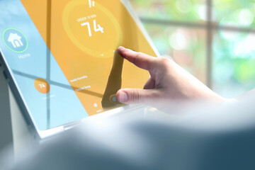Man is Adjusting a  temperature  on the thermostat using a tablet with smart home app