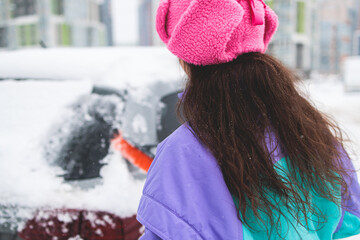 Process of cleaning a car from snow in the morning, girl removing snow from windscreen with a...
