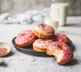 Plate of vanilla cake donuts with pink icing and sprinkles.