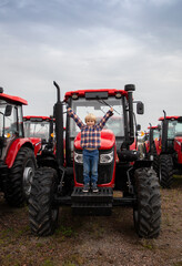 Presentation and sale of new red tractors standing in a row. The child happily stands on a farm...