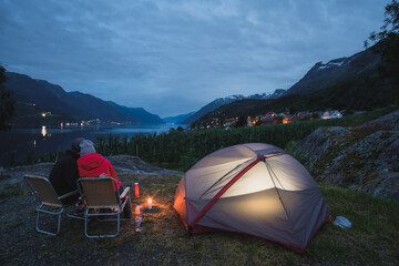couple camping at fjord in Norway, iluminated tent
