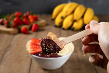 Spoon and a White Bowl of Brazilian Frozen Açai Berry With Paçoca, Strawberry and Banana. on a wooden desk