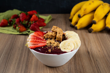 White Bowl of Brazilian Frozen Açai Berry With Paçoca, Strawberry and Banana. on a wooden desk and fruits on background