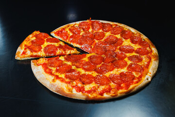Sliced pizza with sausage, tomato sauce, mozzarella, onion and dough rim, topped with cream cheese on a black background