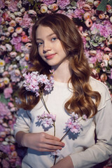 Naklejka premium portrait of a teenage girl with long hair in a white sweater against a wall of flowers.