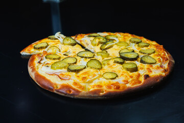 Sliced pizza with cucumber and meat, tomato sauce, mozzarella, onion and edge of dough, filled with cream cheese on a black background