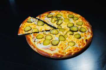 Sliced pizza with cucumber and meat, tomato sauce, mozzarella, onion and edge of dough, filled with cream cheese on a black background