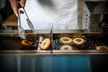 A woman's hand in the process of frying small donuts in the deep oil 