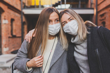 Fototapeta premium Young pretty girls friends in medical masks having fun outdoor in autumn evening in city laughing and going crazy - end of pandemic concept