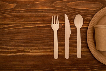 Wooden fork, spoon, knife and cardboard plate and cup on wooden background