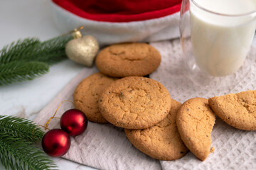 milk and cookies on table with christmas balls and red santa hat