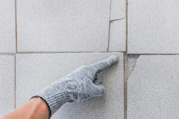 Hand of industrial worker in construction glove points finger on damaged tile floor background....