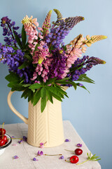 A bouquet of lupines in a jug and a cherry on the table. Garden flowers and berries.