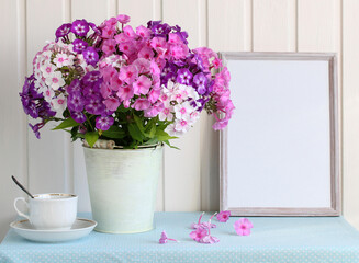 Summer cottage mockup with a bouquet of phlox in a bucket and an empty photo frame on the table.