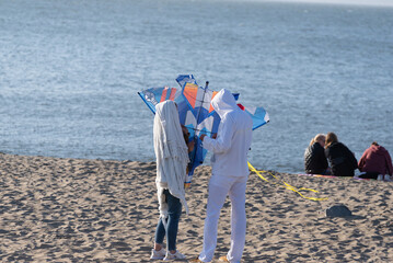 Two people preparing to fly a kite on the beach while two other people sit and talk 
