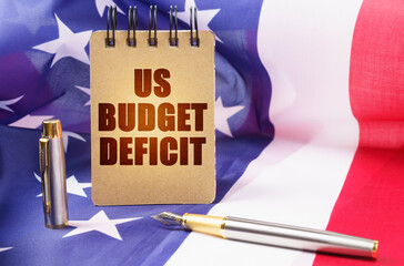 Against the background of the American flag is a notepad with the inscription - US budget deficit - obrazy, fototapety, plakaty