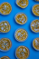 bright sweet tasty orange oranges in white muffin tins sprinkled with white sprinkles on a bright blue background. for menu signage labels for cookbook splash screens