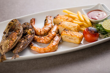 Seafood mix grill with fish tikka, shrimp, prawns, fries, and tomato sauce served in dish isolated on grey background top view of arabic food