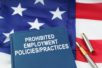 Fototapeta premium On the US flag lies a pen and a book with the inscription - PROHIBITED EMPLOYMENT POLICIES