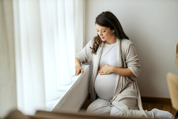 A woman is sitting on a floor next to a cold radiator.