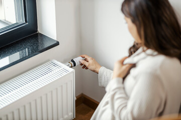 A woman is increases heating on radiator in her apartment.