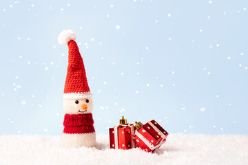Knitted snowman in a red Christmas hat and sweater with two red gifts. Merry Christmas and New Year 2023 greeting card